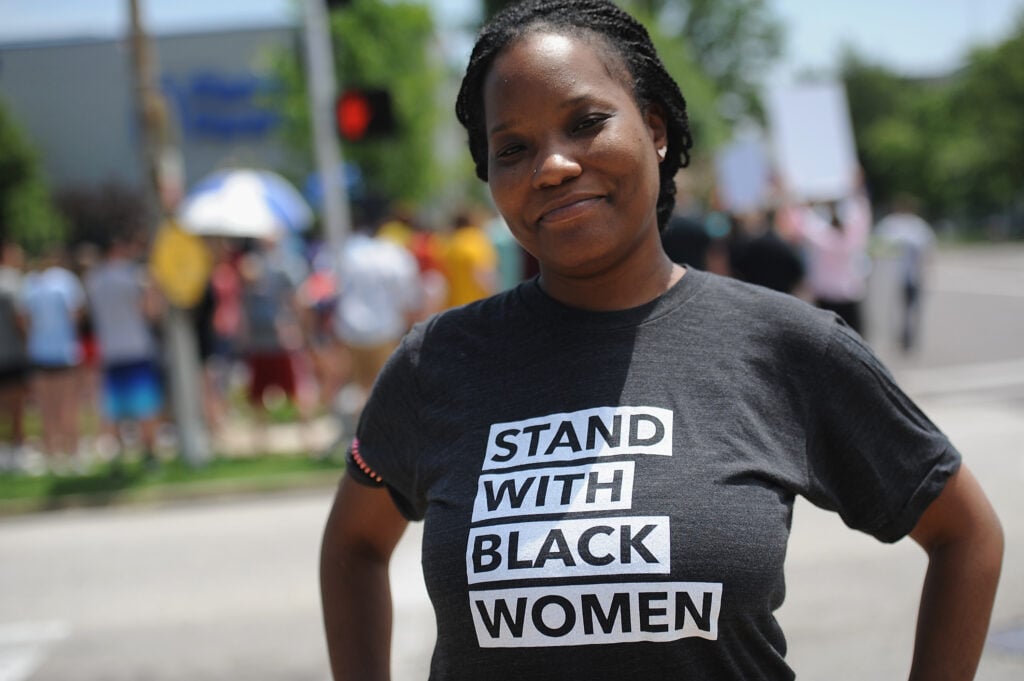 Black woman in "Stand with Black women" t-shirt, theGrio.com